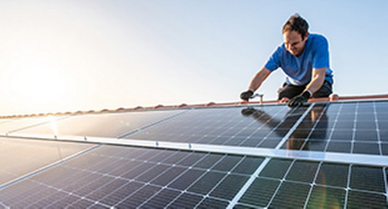 Kneeling professional fixing solar panels from the top of the roof of a house, side view of the roof with sun reflection close-up