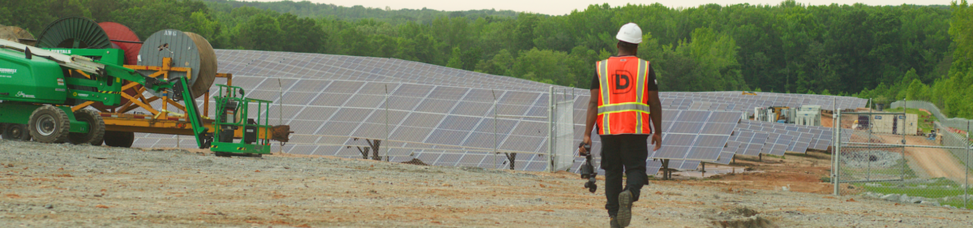 Worker wearing reflective vest and hard hat walking towards solar panels